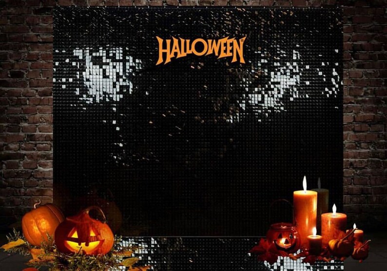 May include: A Halloween display with a black backdrop and the word "HALLOWEEN" in orange. The scene includes lit candles, carved pumpkins, and foliage, creating a festive atmosphere. The backdrop is set against a brick wall.