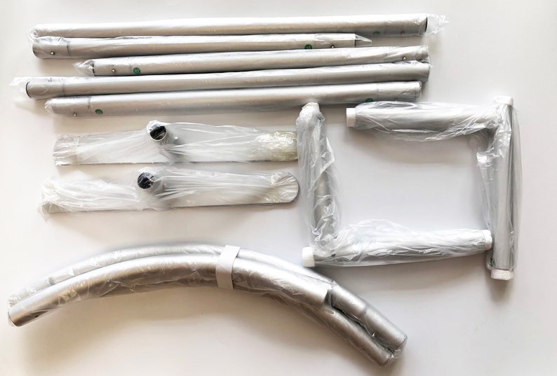 May include: A set of silver metal poles, curved poles, and base plates for a pop-up backdrop stand. The poles are packaged in plastic bags.