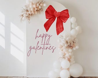 Könnte beinhalten: Weißer Hintergrund mit einer großen roten Schleife mit einem Herz in der Mitte. Der Text "happy galentines" ist in rosa Schrift auf dem Hintergrund geschrieben. Der Hintergrund ist mit weißen und cremefarbenen Ballons und getrockneten Blumen dekoriert.