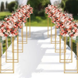May include: Gold metal flower stands with pink and white flower arrangements on each stand. The stands are arranged in two rows, creating a walkway.
