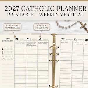 May include: A 2027 Catholic planner printable with a weekly vertical layout. The pages feature September dates, liturgical year details, and saints' feast days. A gold-toned metal ring binder holds the cream-colored paper. A rosary is visible.