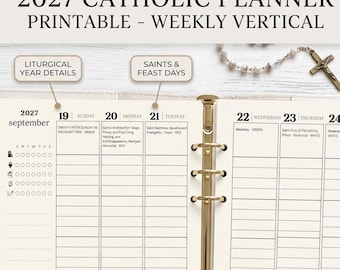 May include: A 2027 Catholic planner printable with a weekly vertical layout. The pages feature September dates, liturgical year details, and saints' feast days. A gold-toned metal ring binder holds the cream-colored paper. A rosary is visible.