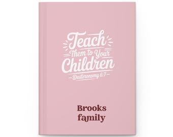 May include: A pink journal featuring the white text "Teach Them to Your Children". The journal also includes the text "Deuteronomy 6:7" and "Brooks family" in a brown font.