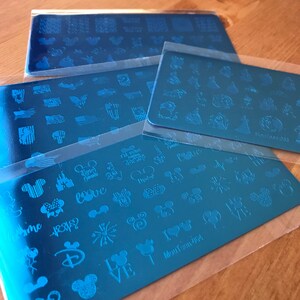 Peut inclure: Quatre plaques de stamping pour ongles en m&eacute;tal bleu avec diff&eacute;rents motifs, notamment Mickey Mouse, des c&oelig;urs, des &eacute;toiles et des drapeaux. Les plaques sont &eacute;tiquet&eacute;es "MouTtoon-964" et "MouTtoon 083".