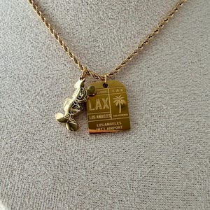 May include: A gold-toned rope chain necklace featuring two pendants: a gold-toned Mickey Mouse silhouette and a rectangular gold-toned tag engraved with LAX, Los Angeles, California, and Los Angeles Int'l Airport, including a palm tree graphic.