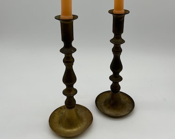 May include: A pair of brass candle holders with a fluted design and a flared base. Each holder has a pale orange candle.