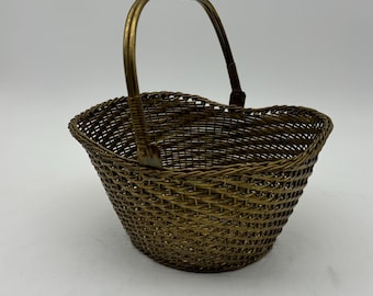 May include: A small, gold-toned, wire basket with a woven design and a handle. The basket is empty.