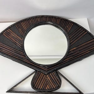 May include: A decorative wall mirror with a circular mirror in the center. The frame is made of dark brown bamboo and has a fan-like shape. The mirror is approximately 18 inches in diameter.