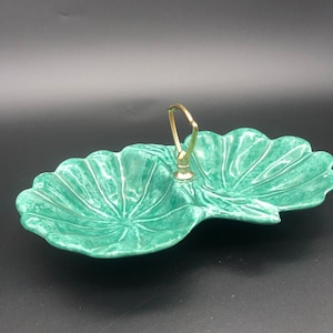 May include: A green ceramic serving dish with two sections and a gold handle. The dish is shaped like a leaf and has a textured surface.
