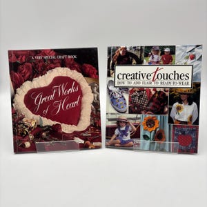 May include: Two craft books are displayed. The first book, "Great Works of Heart," features a red heart design with white trim on the cover. The second book, "creative touches," showcases various craft projects, including decorated shoes and clothing.