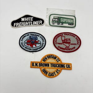 May include: Five embroidered patches featuring trucking themes. One black patch reads WHITE FREIGHTLINER. A green patch in plastic reads SUPERIOR. Two oval patches feature American and California trucking associations. One circular patch reads B.W. BROWN TRUCKING CO.