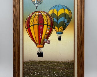 May include: A framed painting of three hot air balloons in the sky. The balloons are red, yellow, blue, and green. The largest balloon has the number "N209" on the side. The painting is set against a background of a field of white flowers.