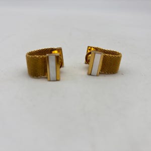 May include: A pair of gold-toned cufflinks with a mesh design. Each cufflink features a rectangular white inlay. The cufflinks are set against a white background.
