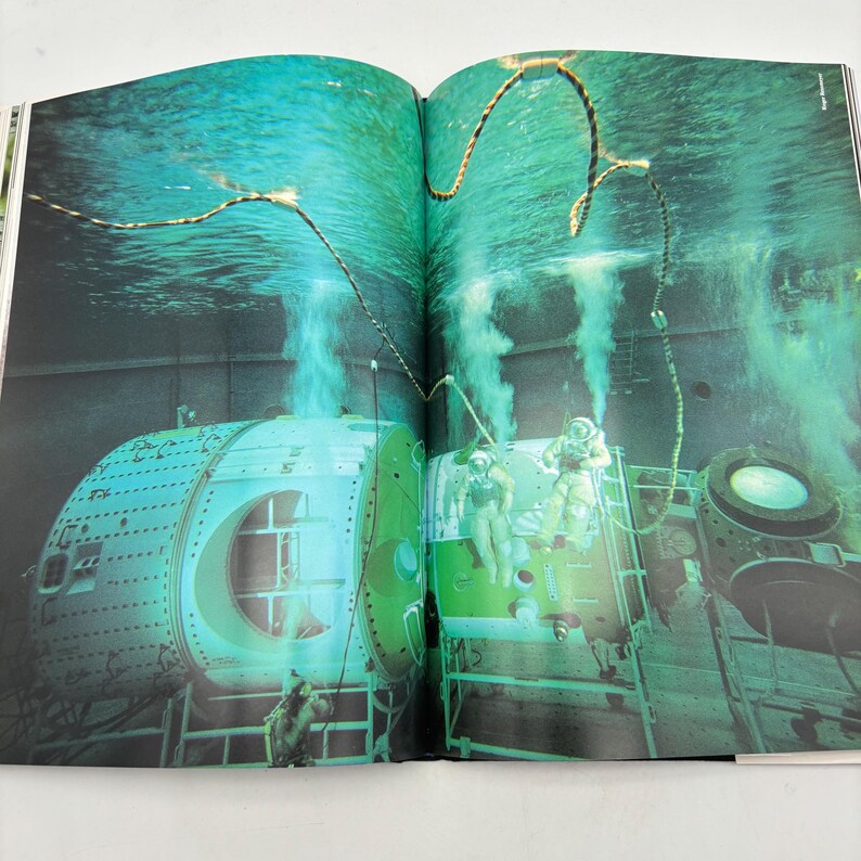 Puede incluir: Una doble p&aacute;gina de un libro abierto muestra una escena submarina con dos estructuras verdes y plateadas similares a submarinos. Se ven dos buzos con trajes de buceo. El agua es de un verde vibrante, con burbujas de aire.