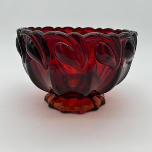 May include: A deep red glass bowl with a scalloped rim and a decorative design of leaves. The bowl has a footed base.