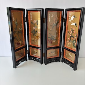 May include: A four-panel folding screen with a black frame and gold-toned panels. Each panel features a different floral and bird design with red and green accents. The screen is a decorative home decor item.