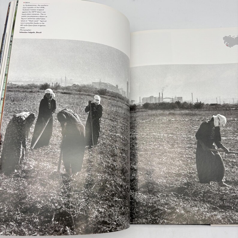 Puede incluir: Fotograf&iacute;a en blanco y negro de varias personas trabajando en un campo. Visten ropa oscura y cubrecabezas, utilizando herramientas. El fondo muestra una zona industrial distante.