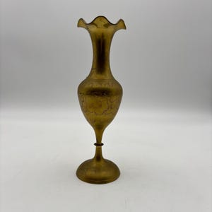 May include: A tall, antique brass vase with a flared, ruffled rim. The vase has a slender neck and a bulbous body with etched floral patterns. It stands on a round base, and the overall height is approximately 12 inches.