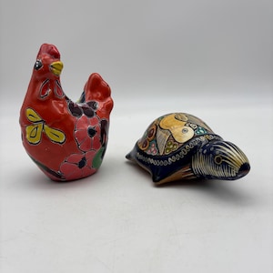 May include: Two ceramic figurines: a red chicken with floral designs and a turtle with a patterned shell. The chicken has yellow, pink, and green accents. The turtle features a blue base with a detailed, colorful shell.