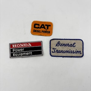 May include: Three rectangular embroidered patches. One is orange with black text reading CAT DIESEL POWER. One is black, white, and red with text reading HONDA power Equipment. One is white with blue border and blue cursive text reading General Transmission.