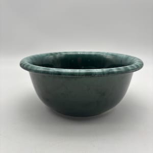 May include: A dark green ceramic bowl with a rounded shape and a slightly textured rim. The bowl has a smooth, glossy finish and is suitable for serving food or as a decorative piece. The bowl's diameter is approximately 8 inches.