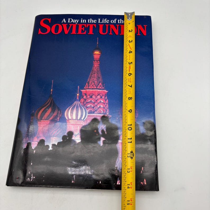 Puede incluir: Un libro titulado "A Day in the Life of the Soviet Union" con una escena nocturna de la Catedral de San Basilio. El libro mide aproximadamente 25 cm de alto, medido con una cinta m&eacute;trica amarilla.