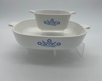May include: Two white ceramic casserole dishes with blue floral designs. The smaller dish is nested inside the larger dish.