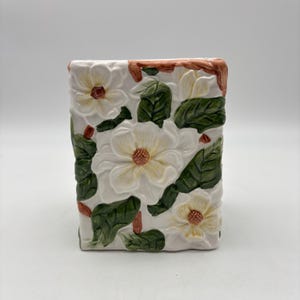 May include: A white ceramic mug with a black handle and the text "But First, Coffee" in a black, handwritten-style font. The mug is on a white surface.