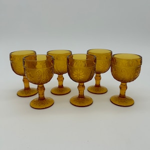 May include: Set of six amber glass goblets with a decorative etched pattern. The goblets have a round bowl and a tall, slender stem.