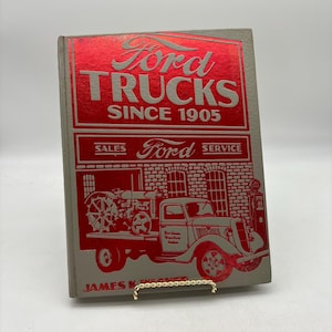 May include: A vintage book titled "Ford Trucks Since 1905." The cover is gray with red lettering and illustrations of Ford trucks and a tractor. The book also has the words "Sales" and "Service" on the cover.