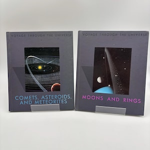May include: Two books titled "Voyage Through the Universe" are displayed. One book is titled "Comets, Asteroids, and Meteorites" and features a colorful illustration of the solar system. The other book is titled "Moons and Rings" and shows a planet with rings.