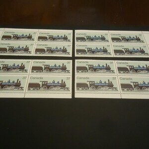 May include: Four sheets of Canadian postage stamps featuring a blue and black steam train with a brown tender. Each stamp has the word "Canada" and the number "37". The stamps are arranged on a black surface.