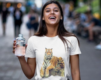 May include: A white t-shirt with a graphic of a tiger sitting on a tree stump. The tiger is orange and black with white stripes. The person wearing the shirt is smiling and holding a clear water bottle.