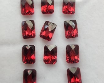 May include: A collection of rectangular, faceted gemstones in shades of red. Each gem has a dark, almost black, top facet and a vibrant red body. The gems are arranged on a white surface.