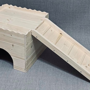 Puede incluir: Un hábitat de madera clara para animales pequeños con una rampa. El hábitat tiene una estructura similar a una casa con un techo festoneado y una entrada arqueada. La rampa facilita el acceso a la parte superior.