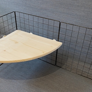 May include: A corner shelf unit featuring a light-coloured wooden shelf and a black wire grid frame. The shelf is supported by a metal frame and designed for corner placement. The design is simple and modern, suitable for various home decor styles.