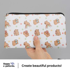 May include: White zippered pouch featuring a repeating pattern of cartoon bears with sunglasses, rainbows, and gifts, interspersed with colorful stars. The pouch is held by a hand. Text at the bottom reads "Create beautiful products!"