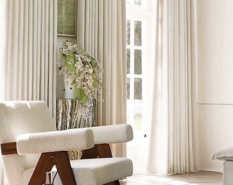 May include: A white armchair with a wooden frame sits in a room with white curtains and a window. The chair is covered in a fluffy white fabric.