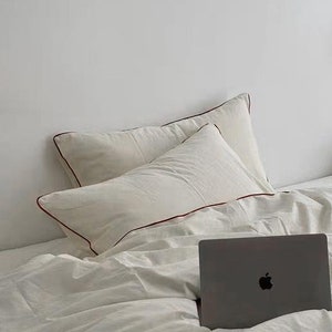 May include: A white bed with a white duvet cover and two white pillows. A laptop computer is on the bed. A white lamp with a white shade is on a white shelf in the background.