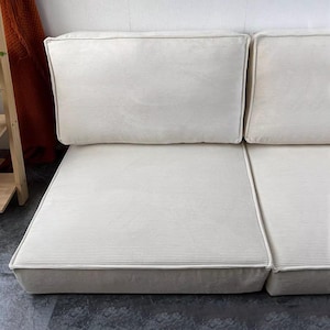 Puede incluir: Sof&aacute; modular color crema con textura de pana. El sof&aacute; presenta un dise&ntilde;o de perfil bajo con cojines rectangulares y una paleta de colores neutros. Los cojines est&aacute;n dispuestos en una configuraci&oacute;n de dos piezas, adecuado para varios espacios.