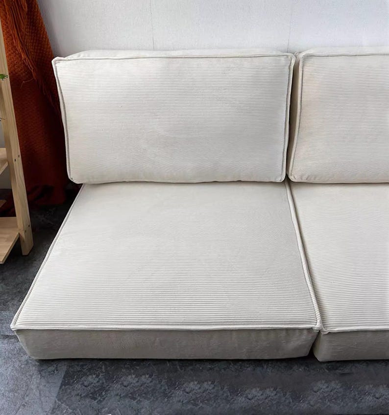 Puede incluir: Sof&aacute; modular color crema con textura de pana. El sof&aacute; presenta un dise&ntilde;o de perfil bajo con cojines rectangulares y una paleta de colores neutros. Los cojines est&aacute;n dispuestos en una configuraci&oacute;n de dos piezas, adecuado para varios espacios.