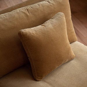 May include: Close-up of three corduroy cushions in a warm, golden-brown hue. The cushions have a ribbed texture and are arranged on a matching corduroy surface, suggesting a cohesive furniture set. The square cushion is in the foreground.