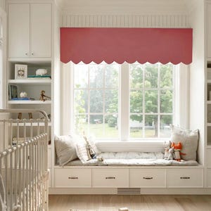 May include: A cozy nursery window seat with a scalloped edge valance in a muted red hue. The window seat features a plush cushion, pillows, and decorative toys. A white crib and built-in shelving complete the inviting space.