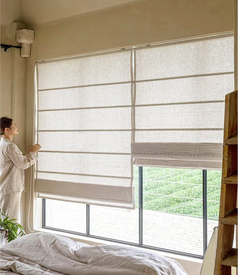 May include: White linen roman shades with a cord pull system, installed in a modern bedroom with a bed and a plant.