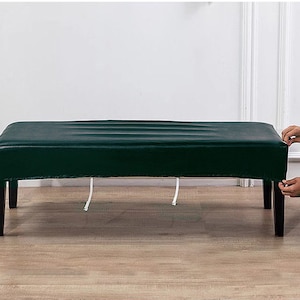 May include: A dark green upholstered bench with black legs. The bench is made of a soft, durable material and has a simple, modern design.