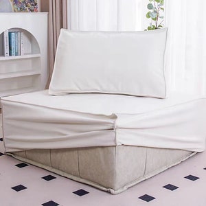 May include: A white upholstered couch with a removable cover. The couch has a light beige base and is sitting on a black and white checkered floor.