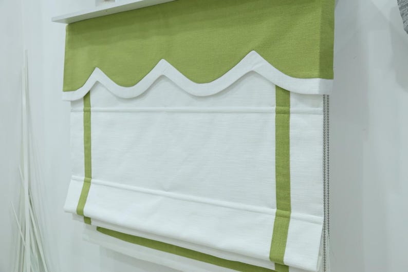 May include: White roman shade with green trim and scalloped valance. The shade has two green stripes along the bottom.