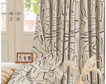 May include: White curtains with a black abstract geometric pattern. The curtains are hung in a living room with a couch, a vase with dried flowers, and a wooden table.