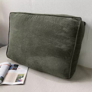 Puede incluir: Un gran cojín de suelo rectangular de pana verde. El cojín está hecho de una tela suave y mullida con una textura ligeramente acanalada.