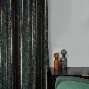 Könnte beinhalten: Ein dunkelgrüner Vorhang mit einem goldenen Chevron-Muster hängt vor einer weißen Wand. Zwei dekorative Glasflaschen, eine braune und eine graue, stehen auf einem schwarzen Regal.